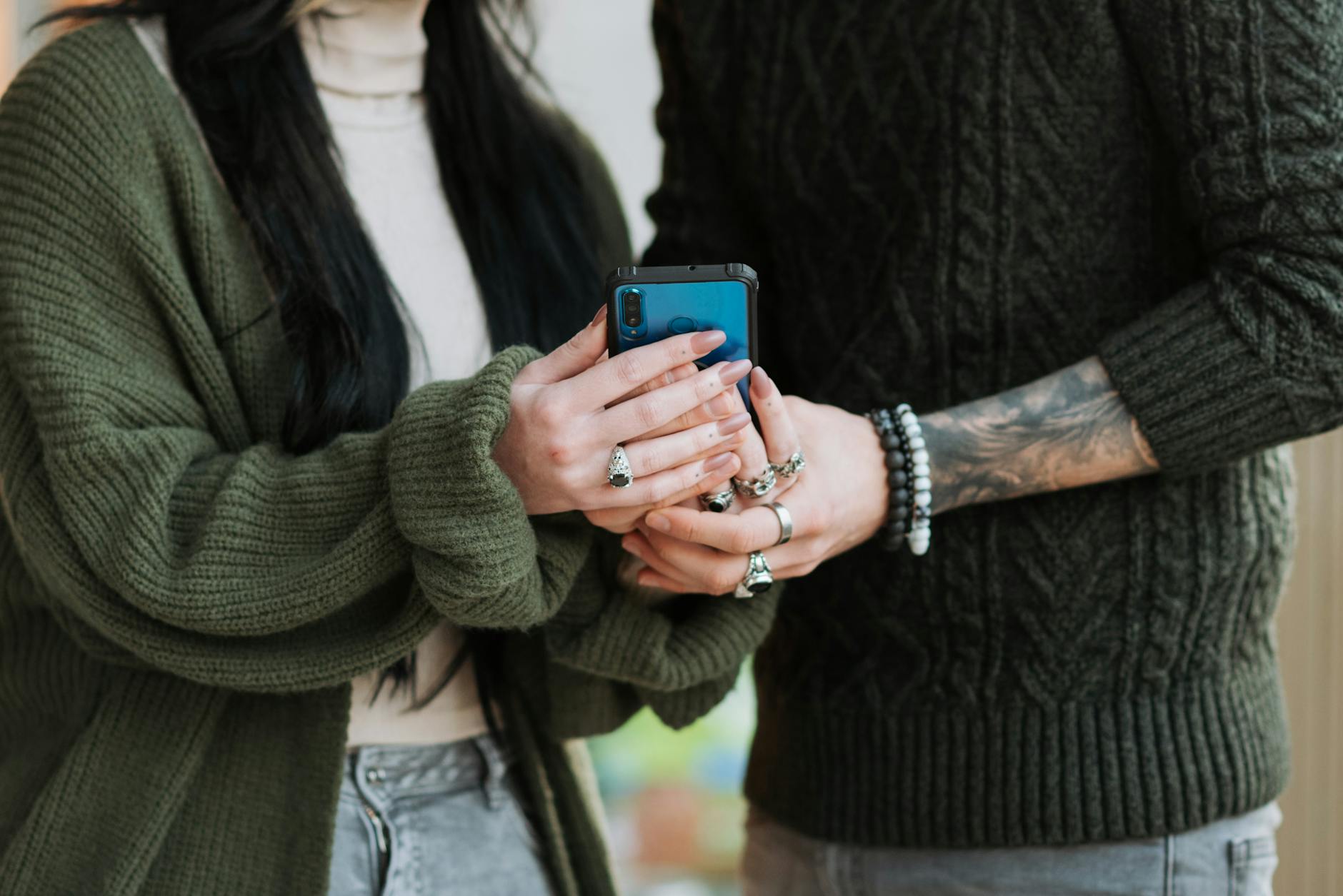 faceless couple in knitwear sharing smartphone in daytime